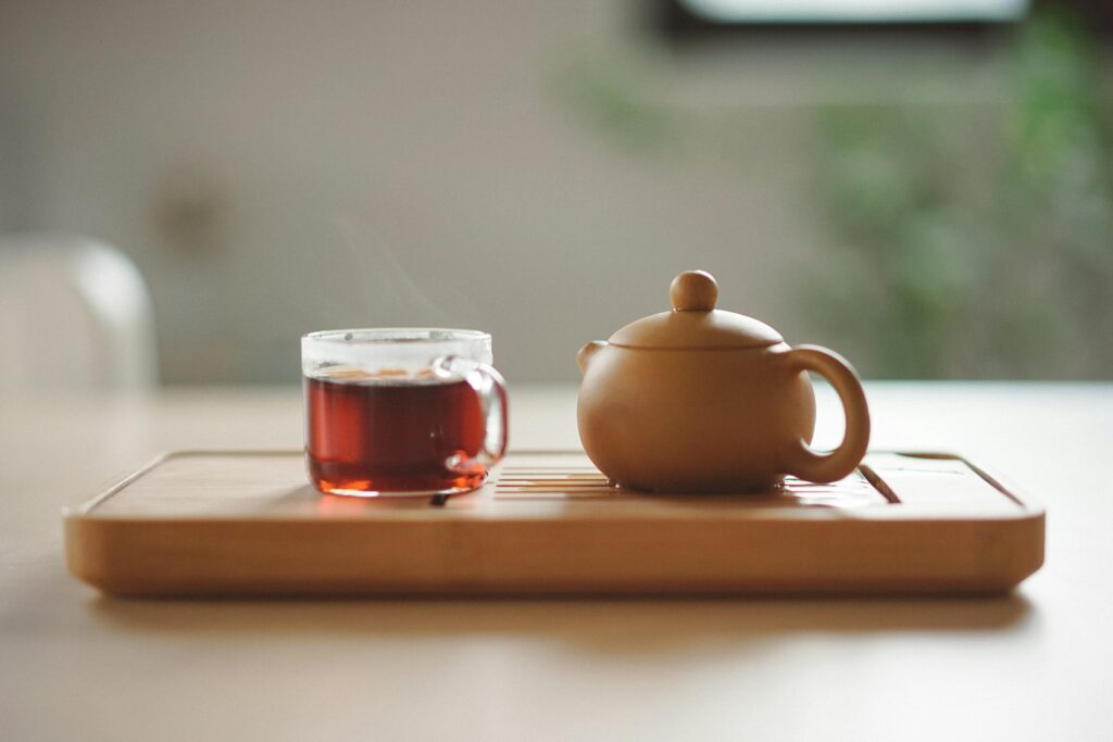 Glass cup of brewed tea next to a ceramic teapot